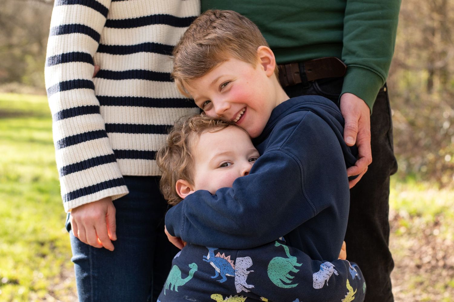 Two siblings cuddling together in front of their mum and dad during an autumn photoshoot