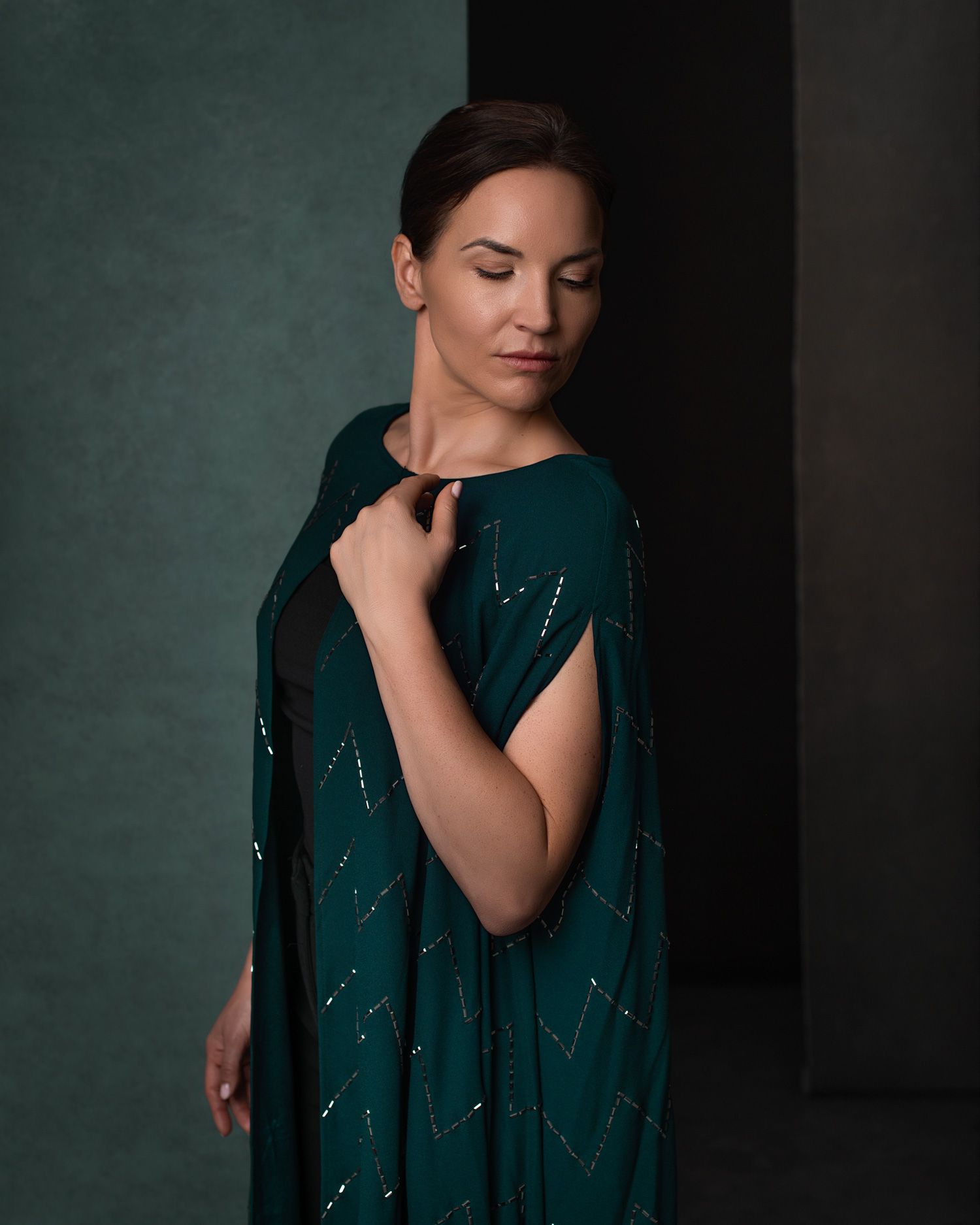 Portrait photo featuring someone wearing an elegant dark teal gown with subtle sparkle detailing against a moody green backdrop.