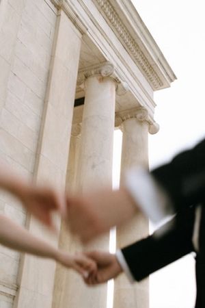 Bride and groom holding hands in front of a grand columned building.