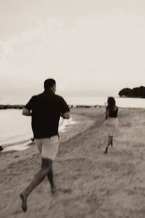 Blurry black and white photo of couple running along shoreline at dusk, motion blur effect.