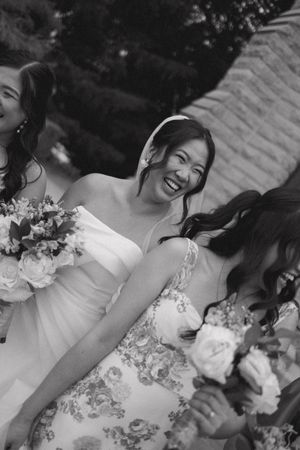 Black and white photo of joyful bride laughing with bridesmaids holding bouquets at outdoor wedding.
