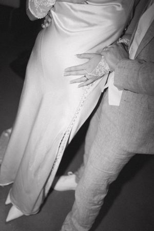Black and white close-up of couple embracing, showing bride's white gown with lace detail and groom's gray suit.