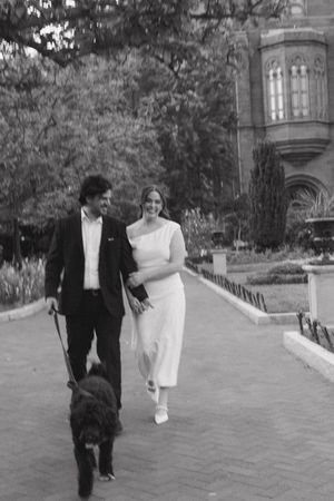 Black and white photo of newlyweds walking their black dog near a historic building.