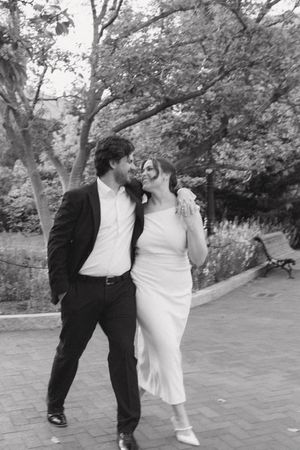 Black and white photo of newlyweds walking and laughing together in a park.