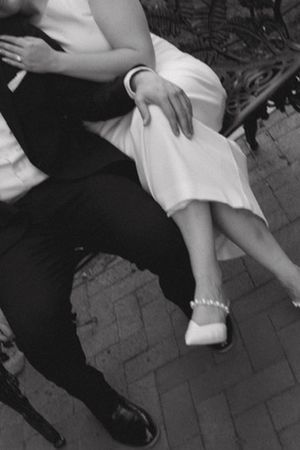 Black and white close-up of a couple sitting together, woman wearing white dress and pearl heels.