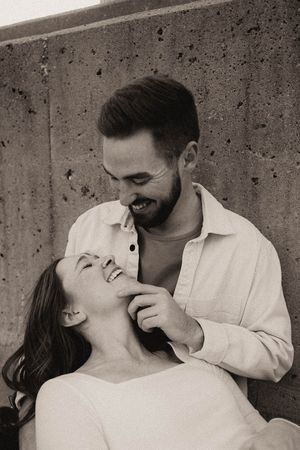 Black and white portrait of smiling couple sharing a tender moment against a concrete wall outdoors.