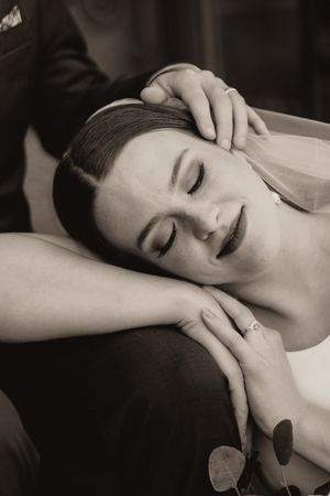 Black and white photo of bride resting head on grooms arm with eyes closed, wearing engagement ring.