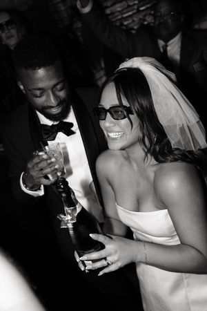 Smiling bride in sunglasses and groom holding champagne at wedding reception.