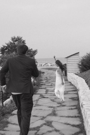 Black and white photo of couple walking toward the sea on a stone pathway.