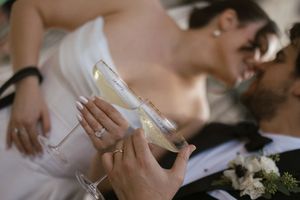 Bride and groom kissing while clinking champagne flutes with wedding florals in the foreground.