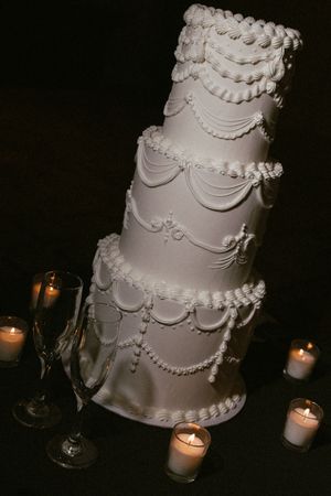 Elegant five-tier white wedding cake with draped fondant details surrounded by candlelight.