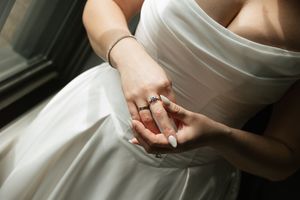 Close-up of bride in white strapless gown showing diamond engagement ring on her finger.