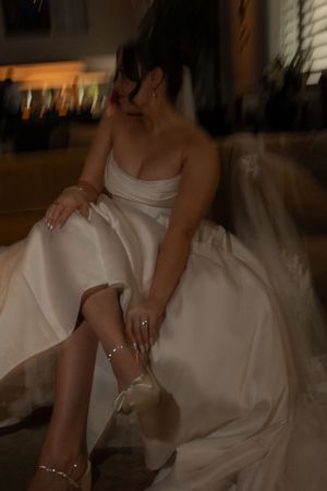 Bride in white ball gown adjusting her jeweled wedding heels while seated.