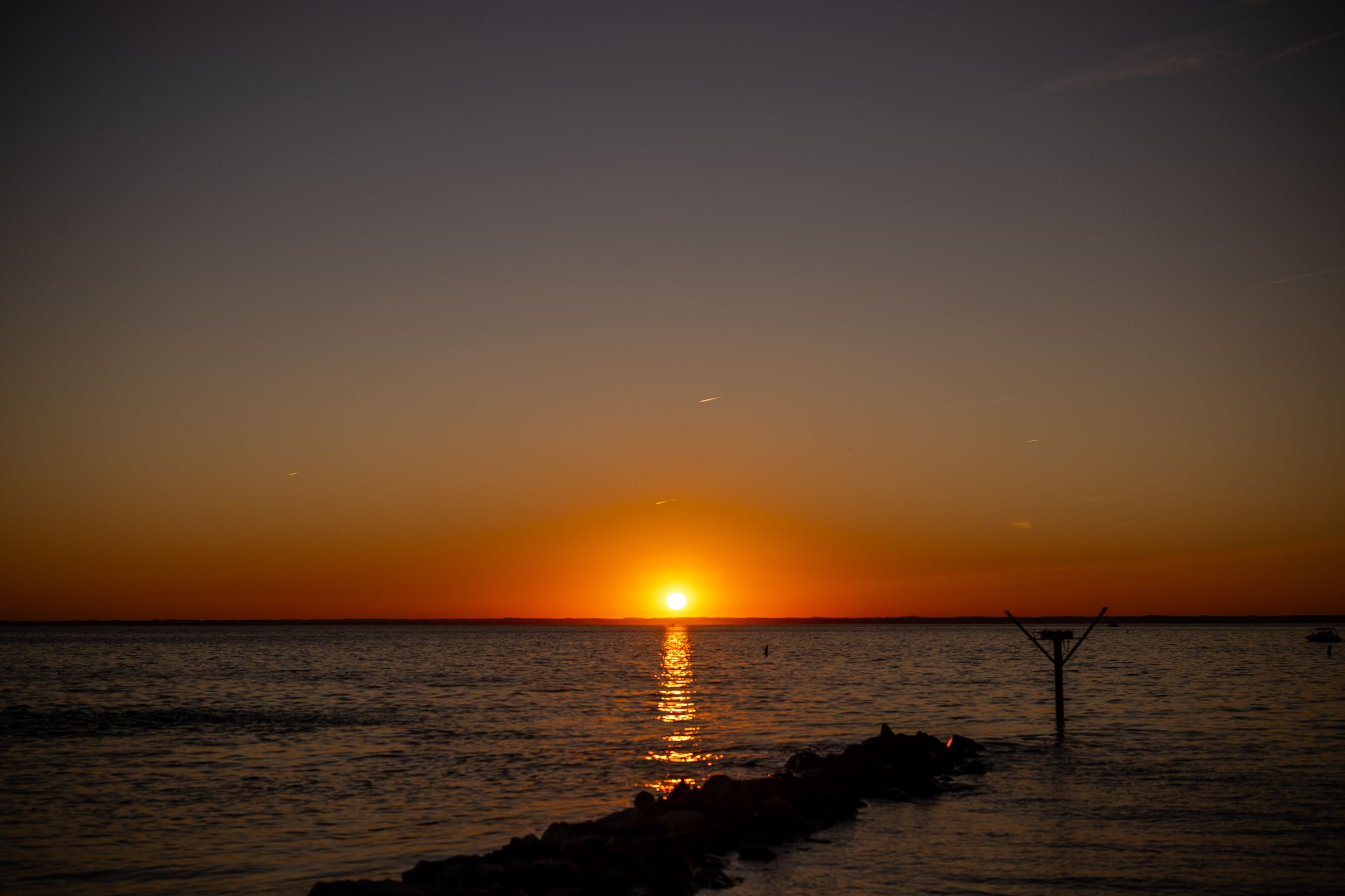 Vibrant orange sunset over calm ocean water with silhouetted pier.