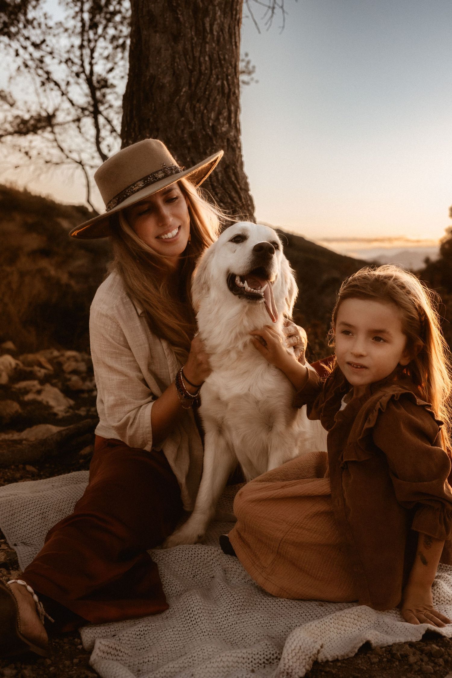 A happy white dog in Javea  sits with companions on a blanket at sunset, creating a warm and intimate family moment. Javea photographer