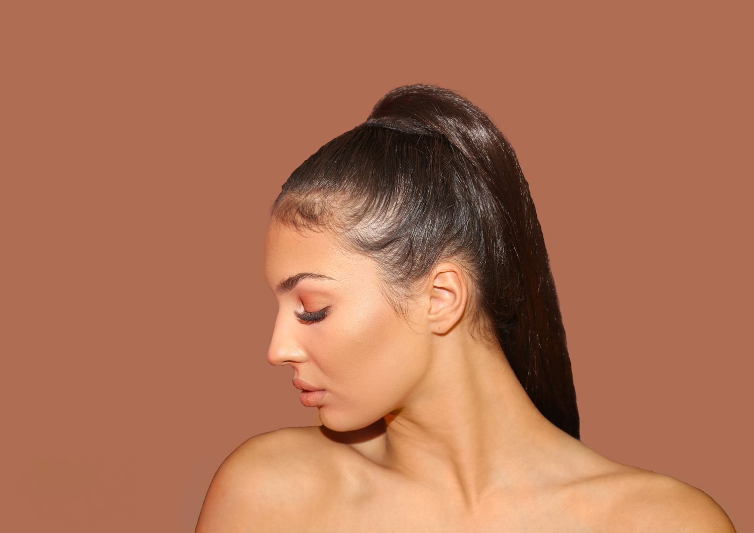A profile view of someone with sleek dark hair in a ponytail against a brown background.