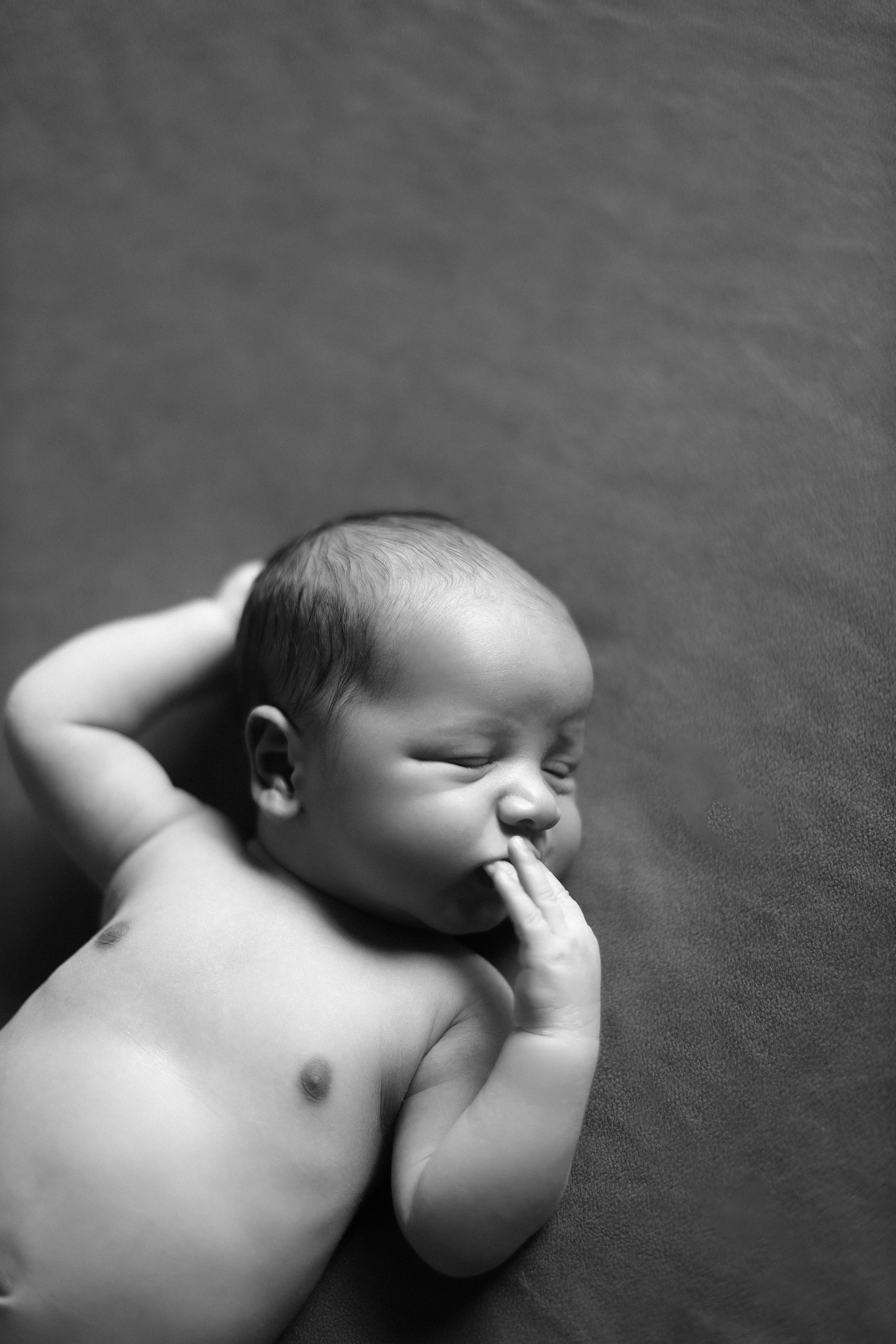 Peaceful sleeping newborn baby in black and white with hand near mouth.