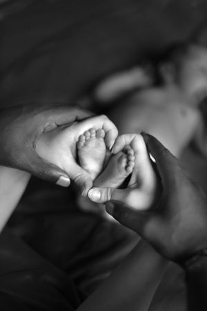 Close-up black and white photo of tiny baby feet being gently held by adult hands.