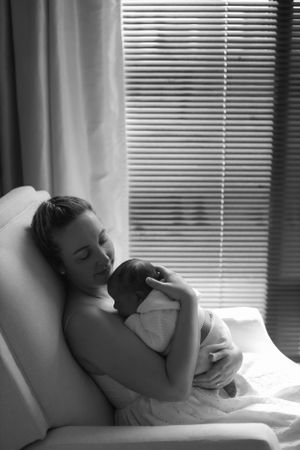 Mother resting in hospital chair holding newborn baby in peaceful black and white photograph.