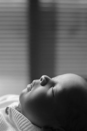 Profile view of sleeping baby in black and white with window light creating soft shadows.
