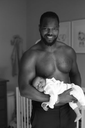 Proud parent holding sleeping newborn baby in black and white nursery portrait.