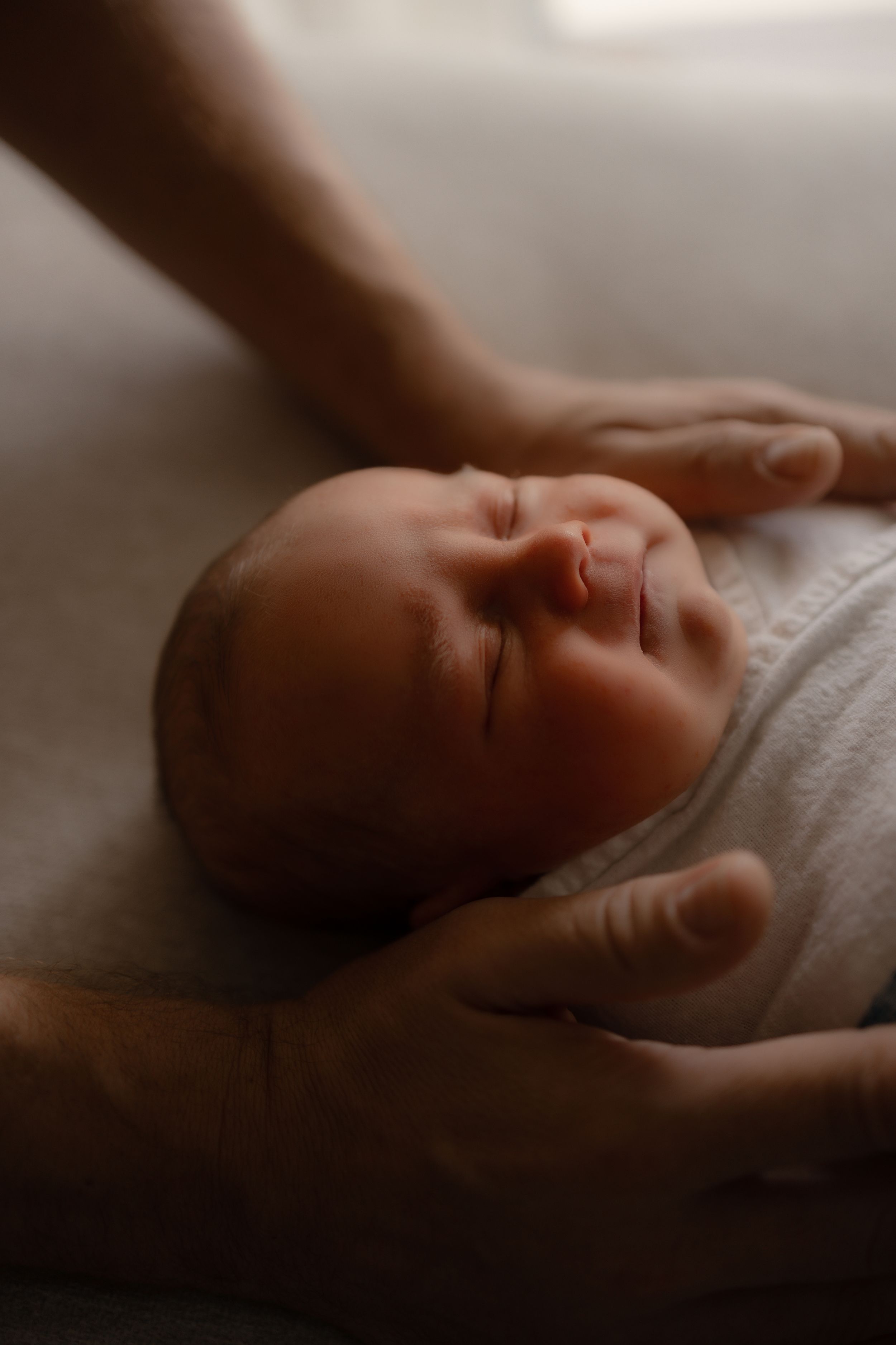 Gentle hands holding a peaceful sleeping newborn in moody lighting.