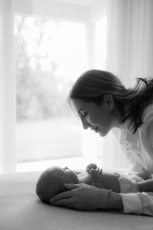 Parent leaning over newborn baby lying on soft surface in gentle black and white portrait.