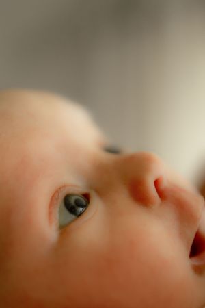 Extreme close-up of a baby's face showing bright blue eye and tiny nose in soft focus.
