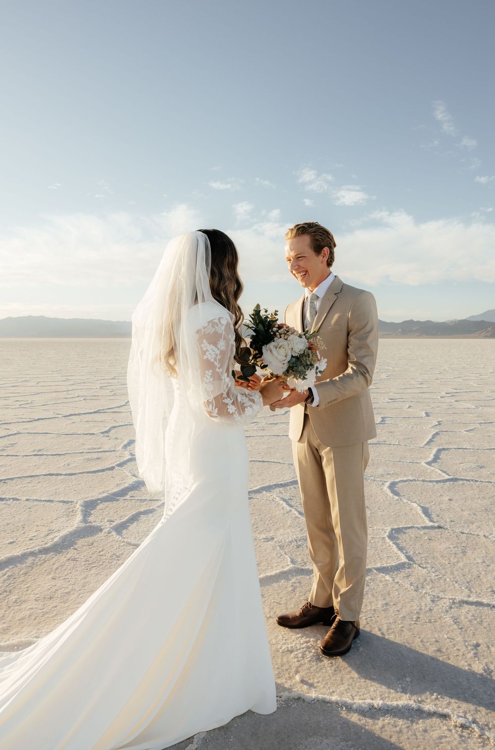 Bride and groom face each other holding a bouquet on the Bonneville Salt Flats with mountain views.