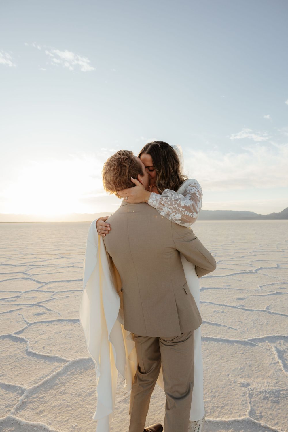 Couple shares a romantic kiss on the expansive Bonneville Salt Flats at golden hour sunset.