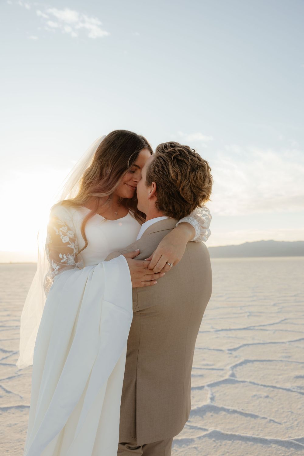 Bride and groom lean in for a kiss bathed in warm golden sunset light on the salt flats.