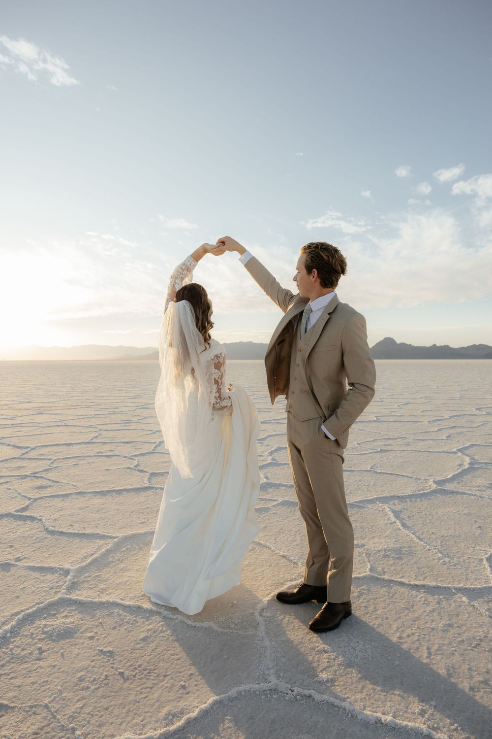 Bride and groom dance together on the Bonneville Salt Flats, arms raised under a glowing sky.
