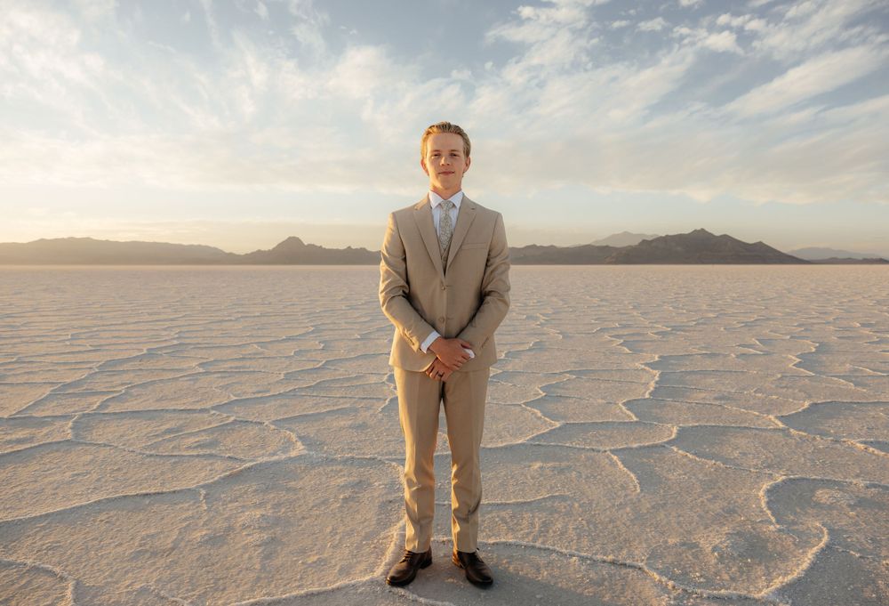 Groom stands confidently in a tan suit on the expansive Bonneville Salt Flats with mountain backdrop.