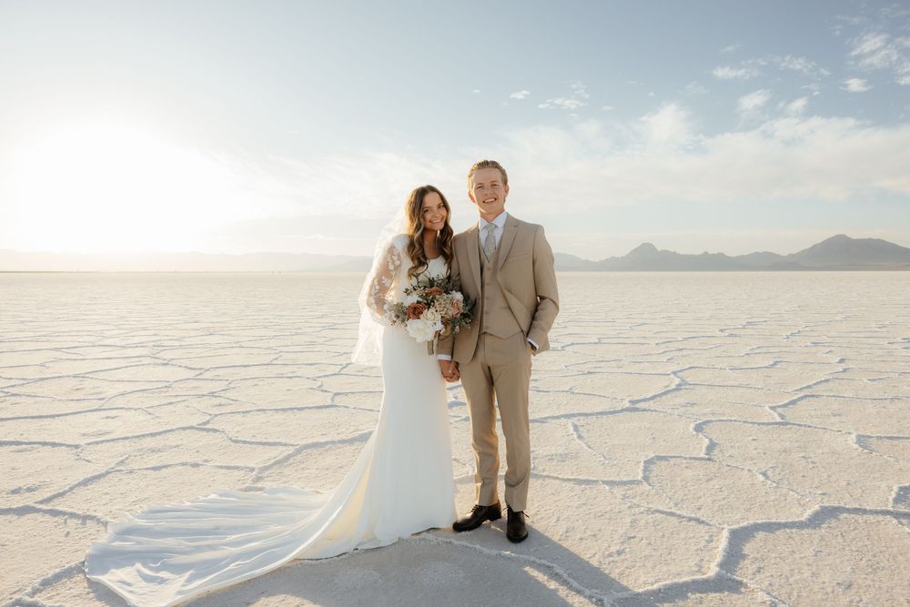 Bride and groom stand together holding bouquet on the Bonneville Salt Flats with mountains in background.