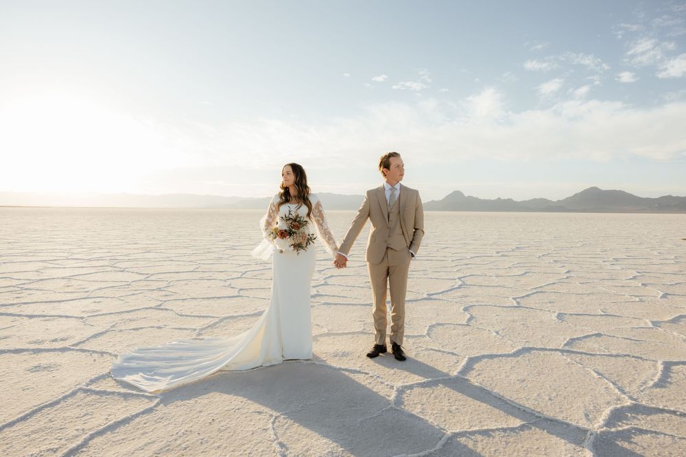Newlyweds hold hands and walk across the expansive white Bonneville Salt Flats in wedding attire.
