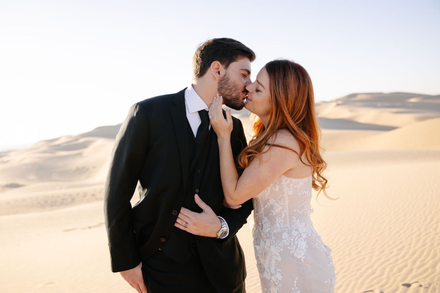 Intimate moment between couple in wedding attire on desert sand dunes.