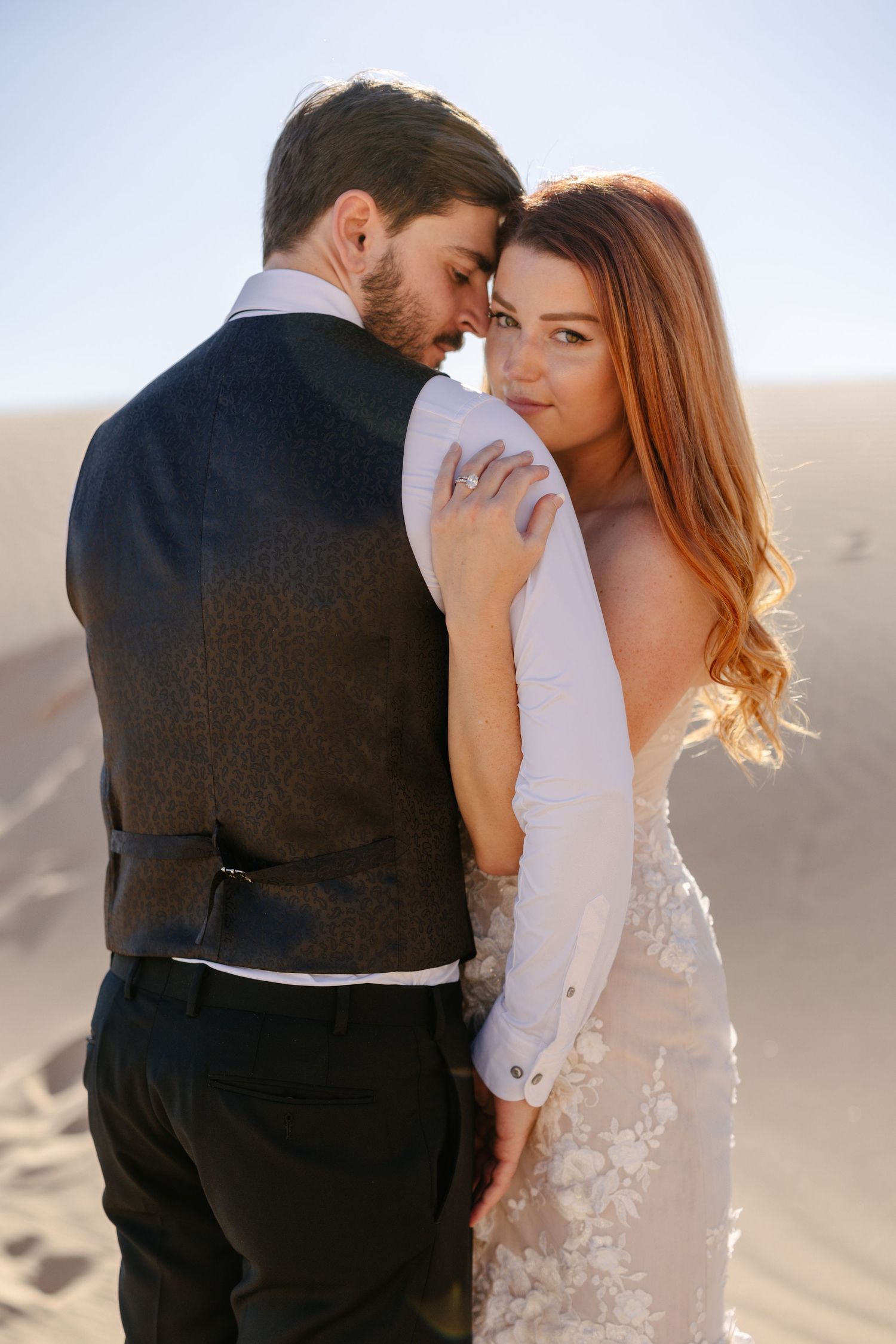 A romantic wedding photo of a couple embracing on desert sand dunes.