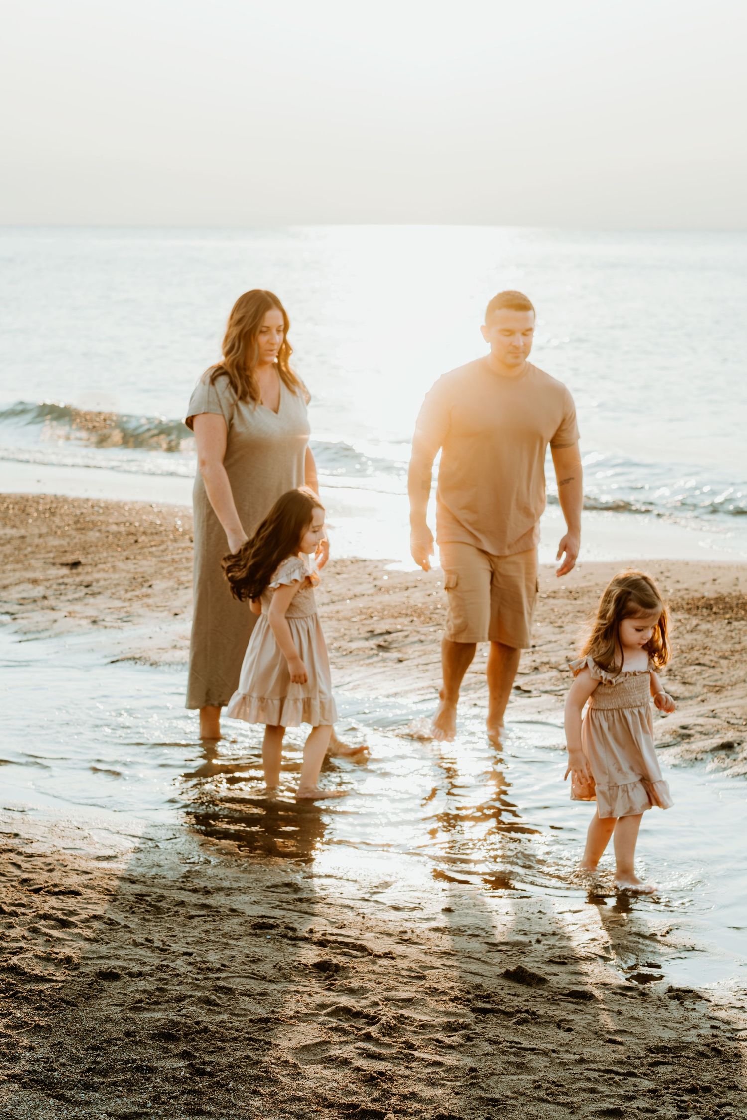 Family walking along beach shoreline during golden sunset hour.