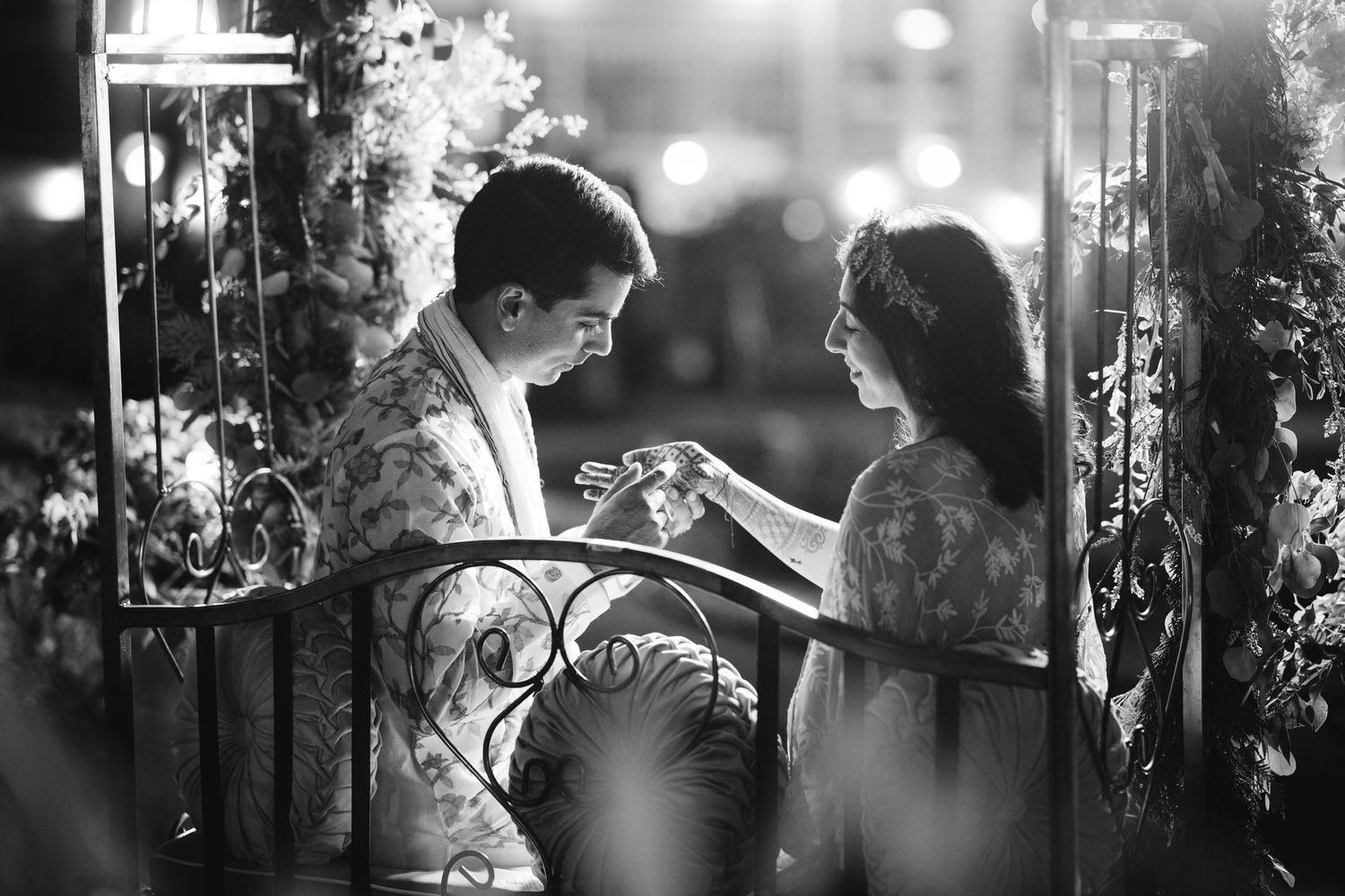 Intimate black and white moment of a South Asian couple during their wedding, surrounded by floral decor and soft romantic lighting.