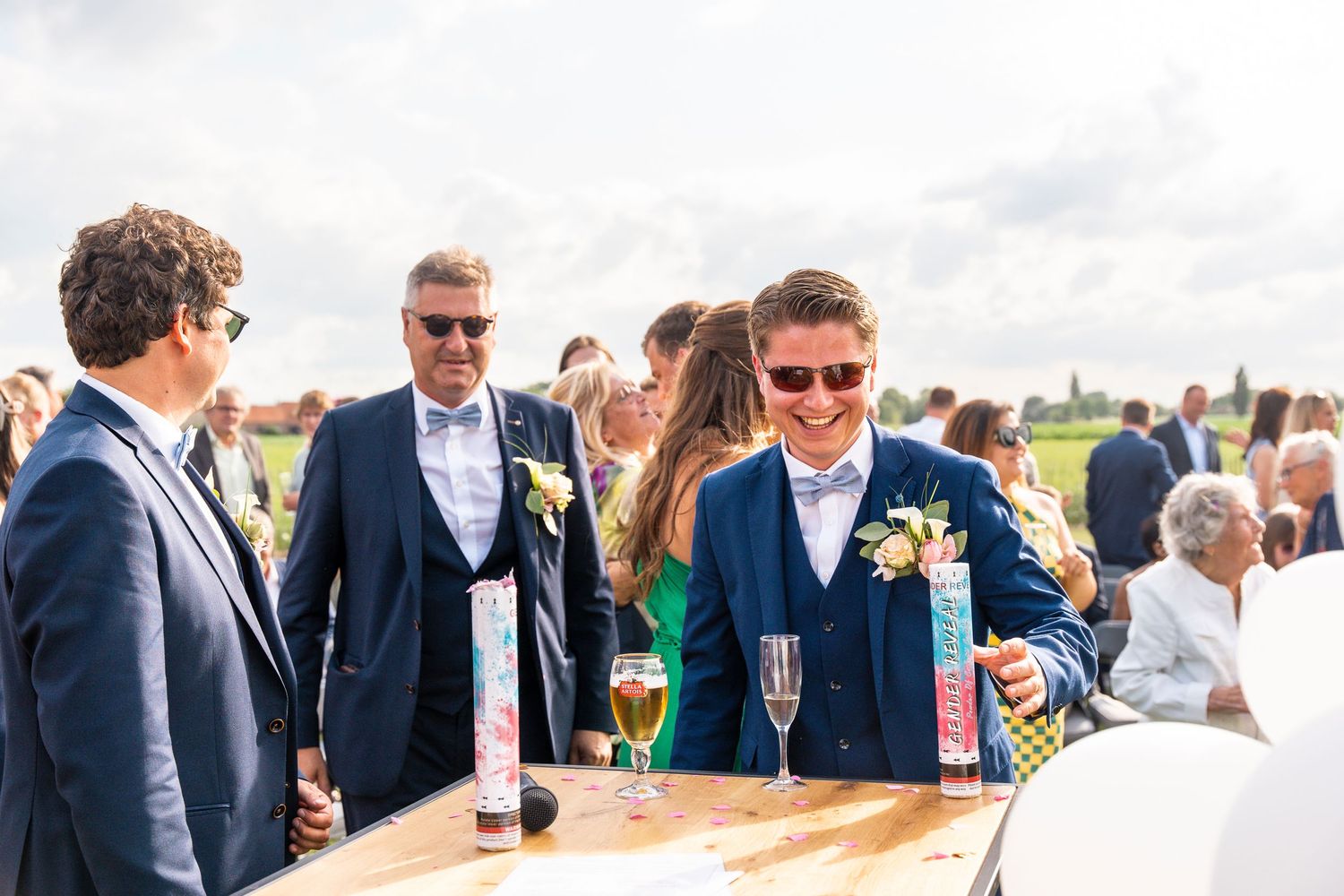 Guests mingling at outdoor reception with drinks near rustic wooden bar.