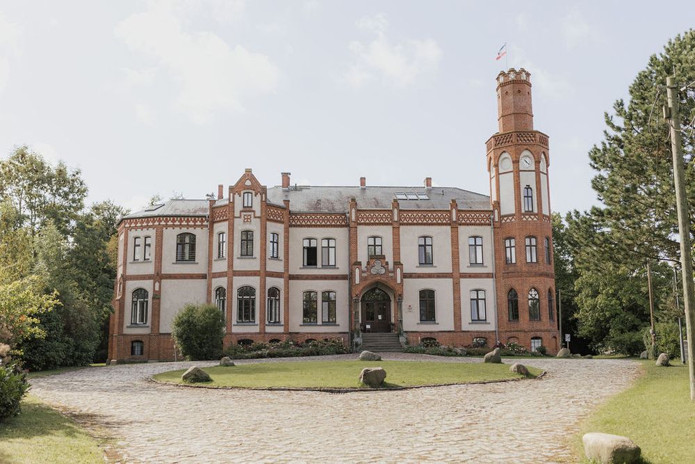 Panoramic view of a historic red brick Victorian mansion with tower and architectural details set on a hilltop.
