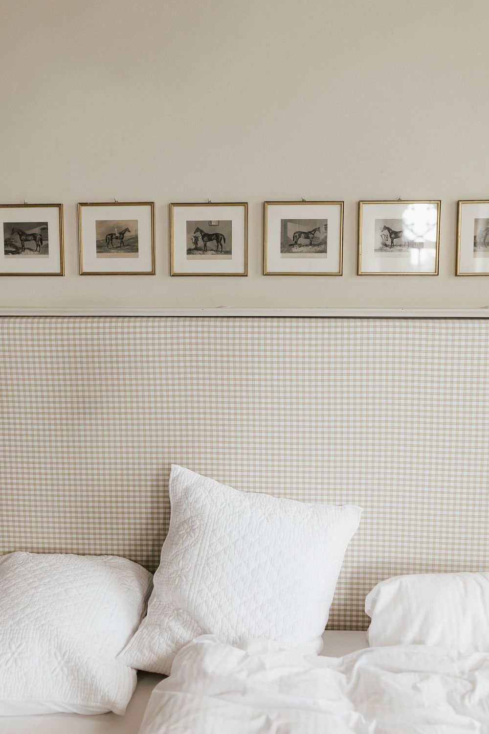 A minimalist bedroom wall with a row of framed photographs above a white bed with multiple pillows.