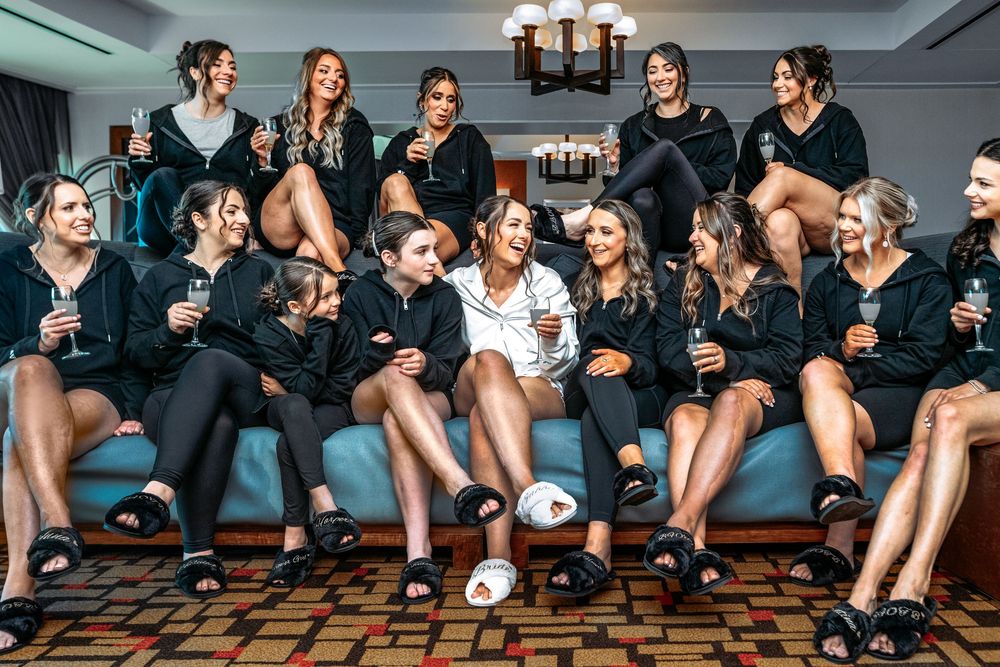 Athletes in black workout attire sit in a row on a wooden floor during a team meeting or training session.