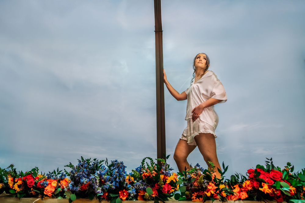 A person in a pink top dances joyfully against a cloudy sky and colorful floral backdrop.