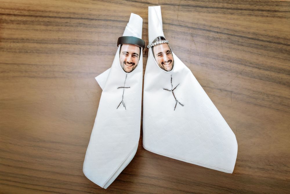 Two white paper napkins folded into shapes with stick figure drawings on a wooden table surface.