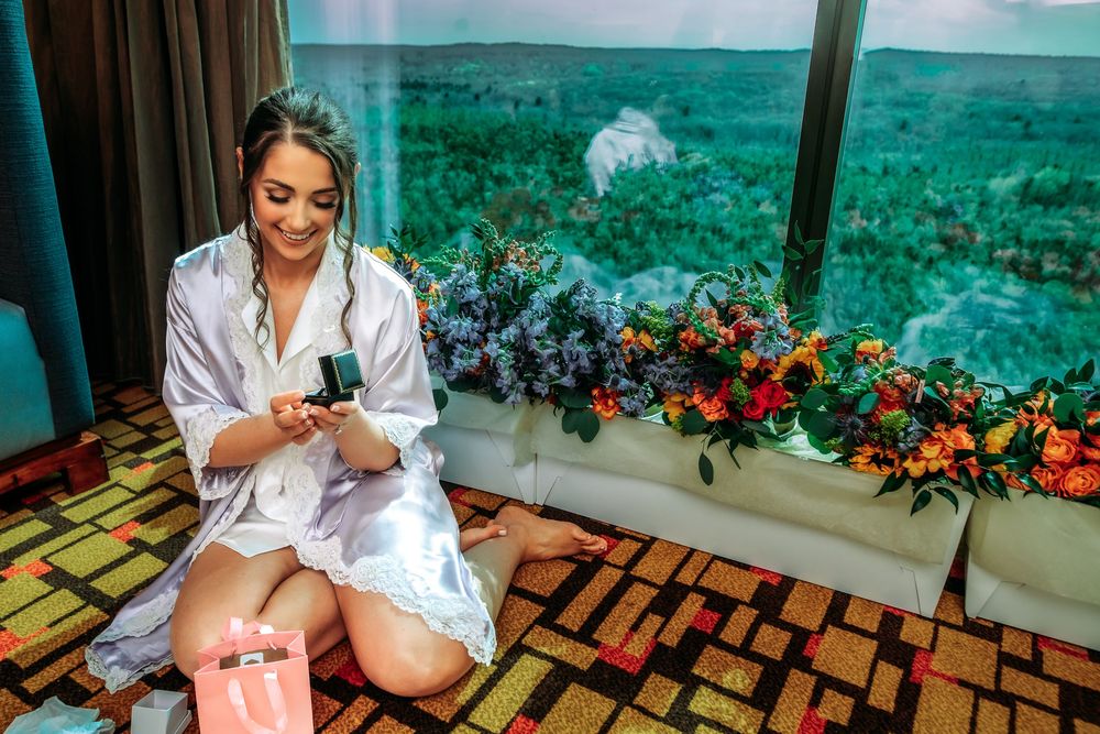 A person in a white robe sits on a wooden bench against a tropical backdrop with vibrant floral arrangements.