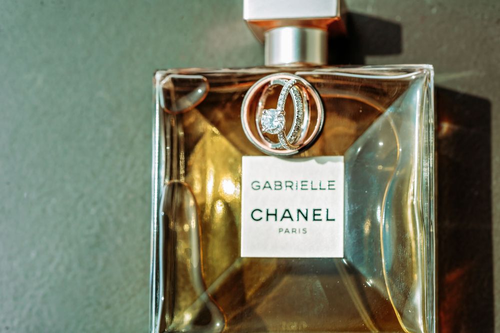 A glass bottle of Gabrielle Chanel perfume with golden liquid inside sits against a green background.