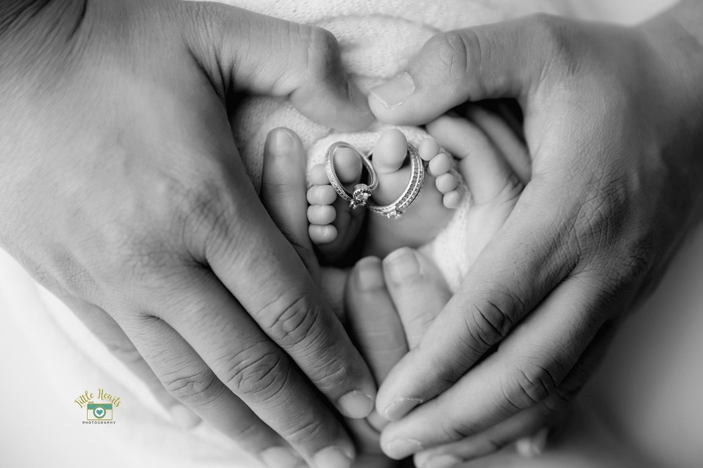 Black and white close-up image of two hands gently holding a sleeping newborn baby.