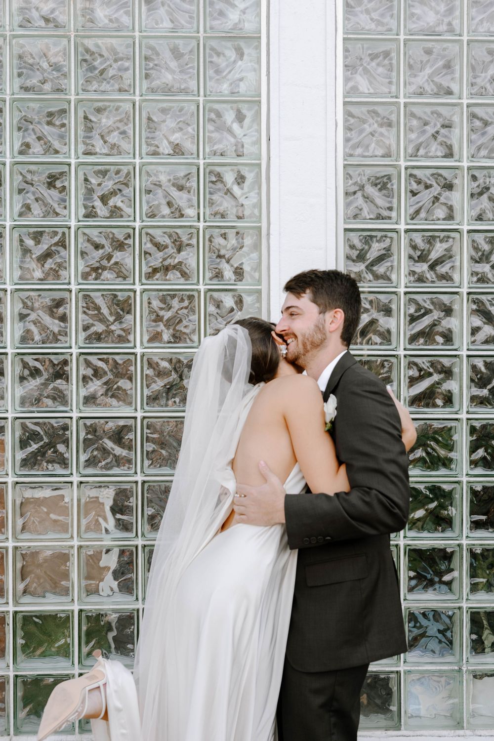 A couple shares an intimate moment in front of a glass block wall during their wedding photoshoot.