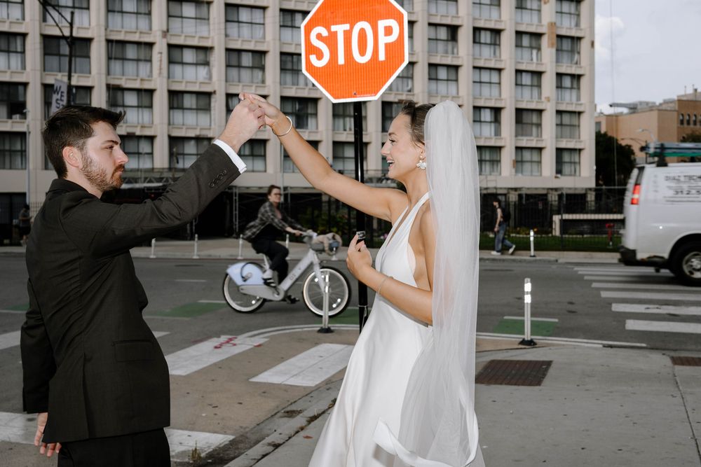 Wedding couple poses playfully near an orange stop sign on a city street.